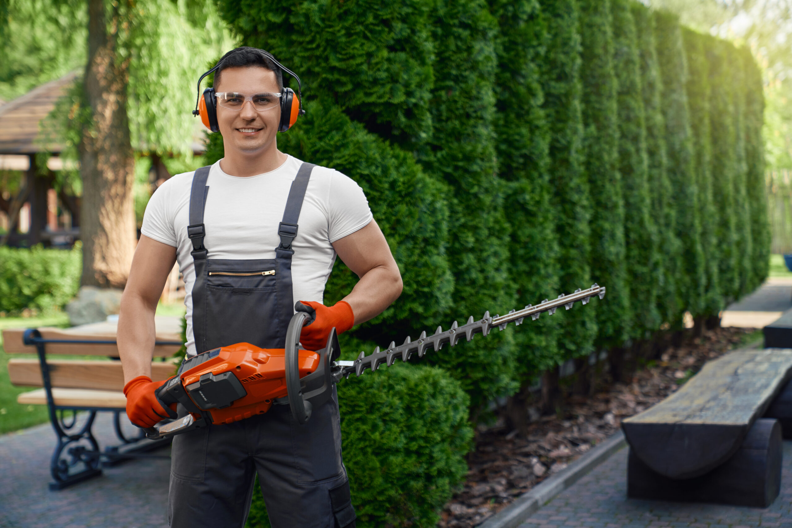 Man in overalls holding hedge trimmer while posing at garden
